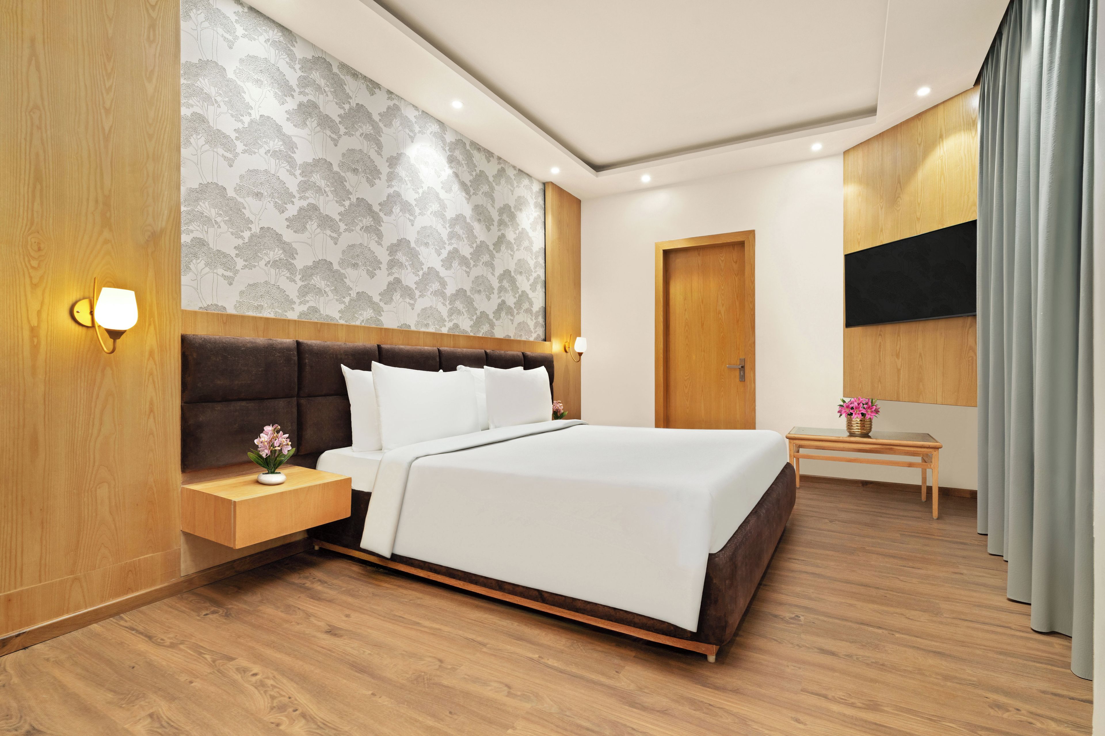 Habitación de hotel moderna con una cama grande, una mesita de noche con lámpara, cabecero de madera y una pared con estampado de árbol.