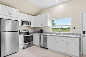 A modern kitchen with stainless steel appliances, white cabinetry, and a window offering a view of the outdoors.
