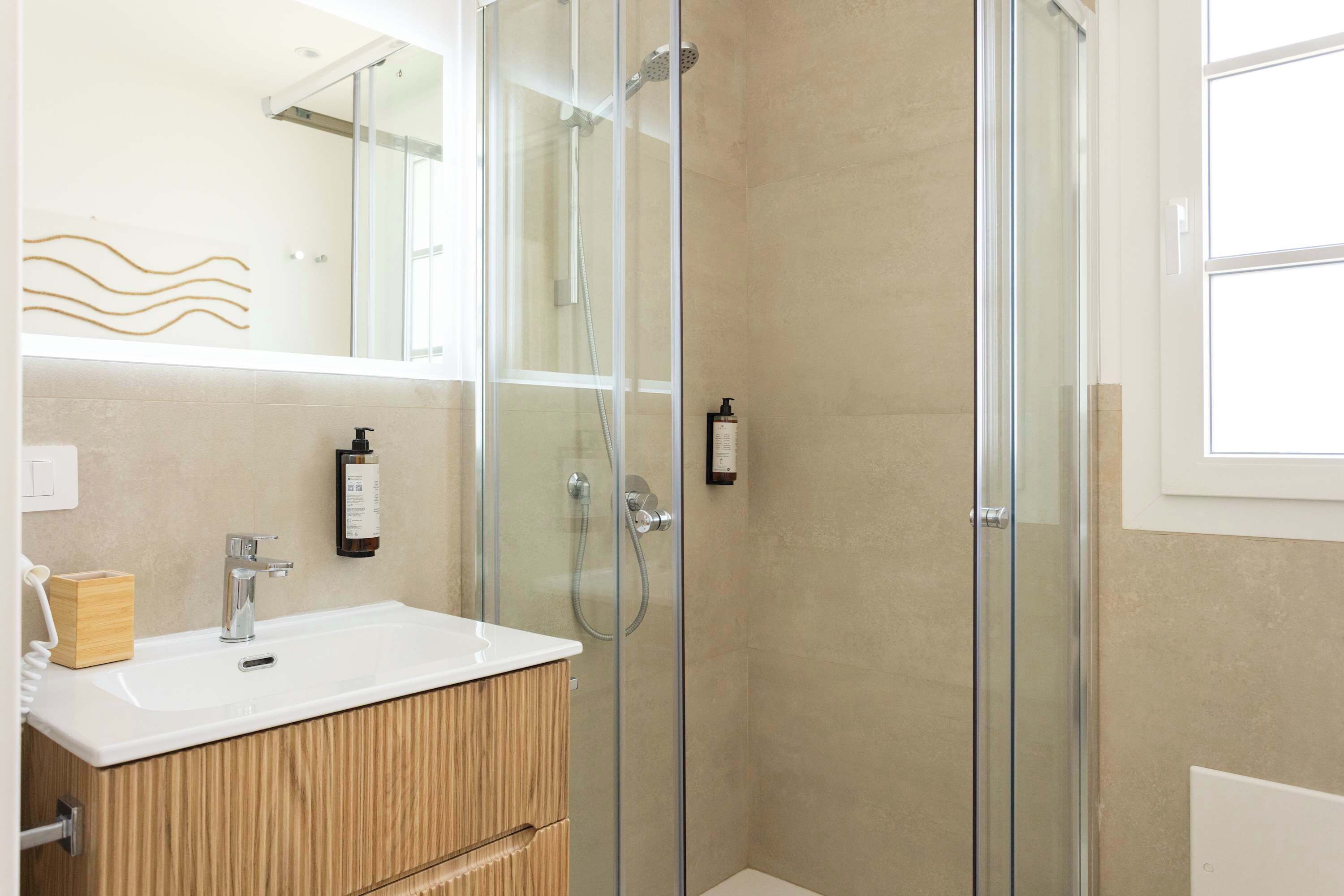 Un baño moderno con cabina de ducha de vidrio, tocador de madera y un espejo grande.