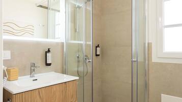 Un baño moderno con cabina de ducha de vidrio, tocador de madera y un espejo grande.