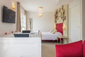 Een hotelkamer met een bed, een bureau, een spiegel, een televisie en een rode stoel.