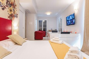 Een hotelkamer met een bed, een rood hoofdeinde, een aan de muur bevestigde televisie, een badkamer met een wastafel en spiegel, en een rode fauteuil.