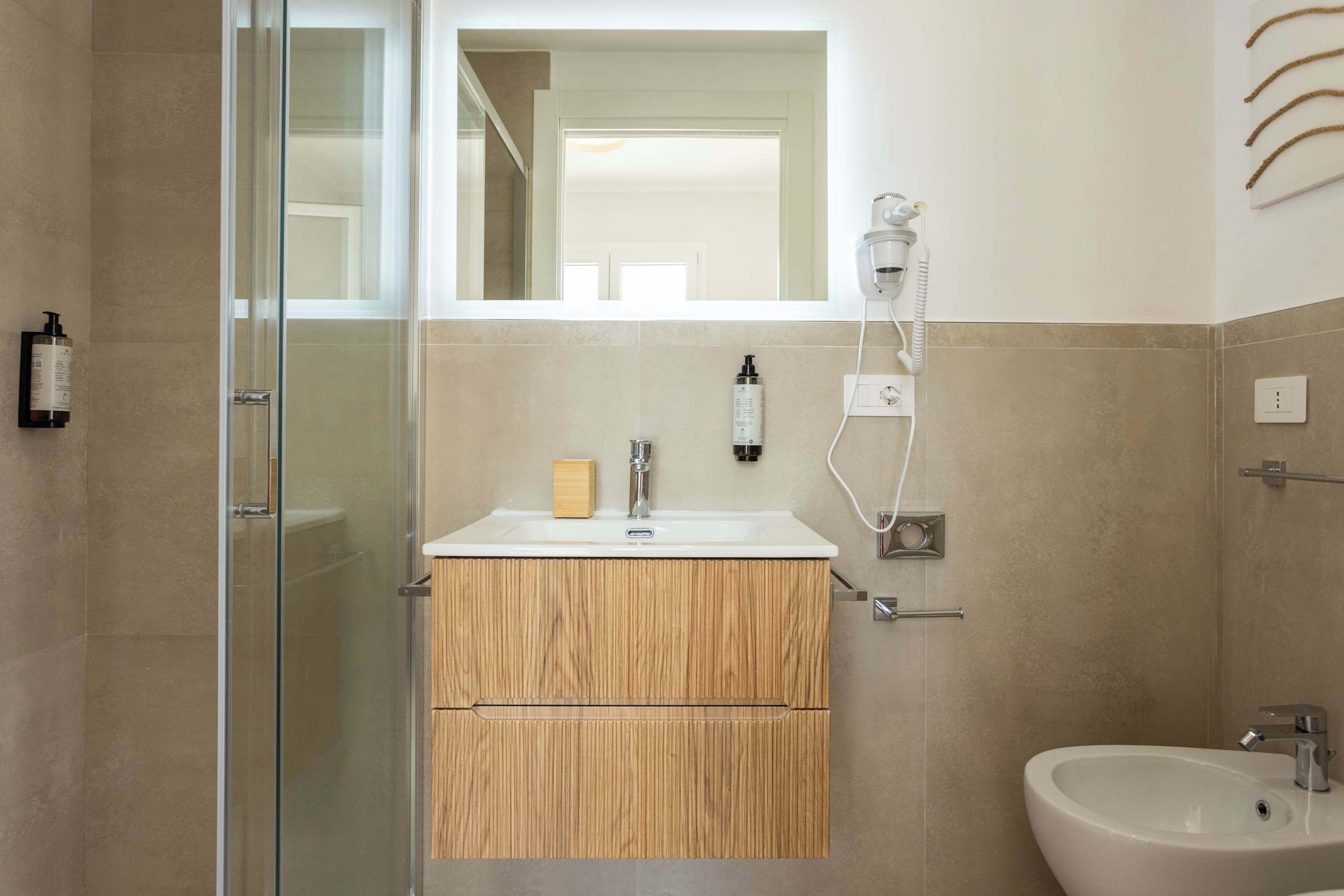 A modern bathroom with a glass shower enclosure, a wooden vanity, a white sink, and a mirror above the vanity.