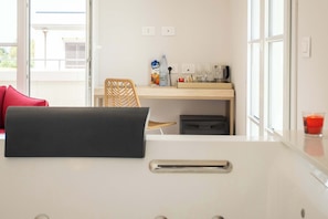 Een moderne keuken met een wit aanrecht, een rode stoel, een houten stoel, een koffiezetapparaat en een waterfles.