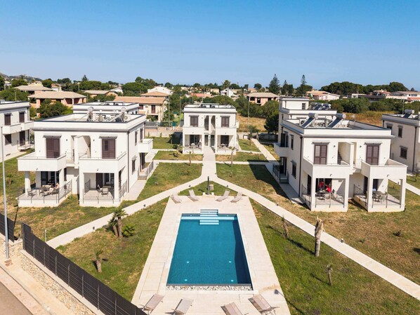 Ein Wohnkomplex mit moderner Architektur, einem zentralen Schwimmbecken und einem gepflegten Rasen.