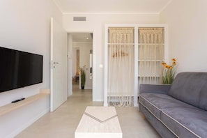 A living room with a flat-screen TV, a grey sofa, a coffee table, and a macrame curtain. - Appartamento "Isola di Marettimo 2" (Carini)