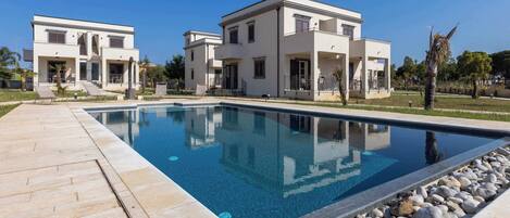 Una casa moderna de dos pisos con piscina, terraza pavimentada y jardín ajardinado.