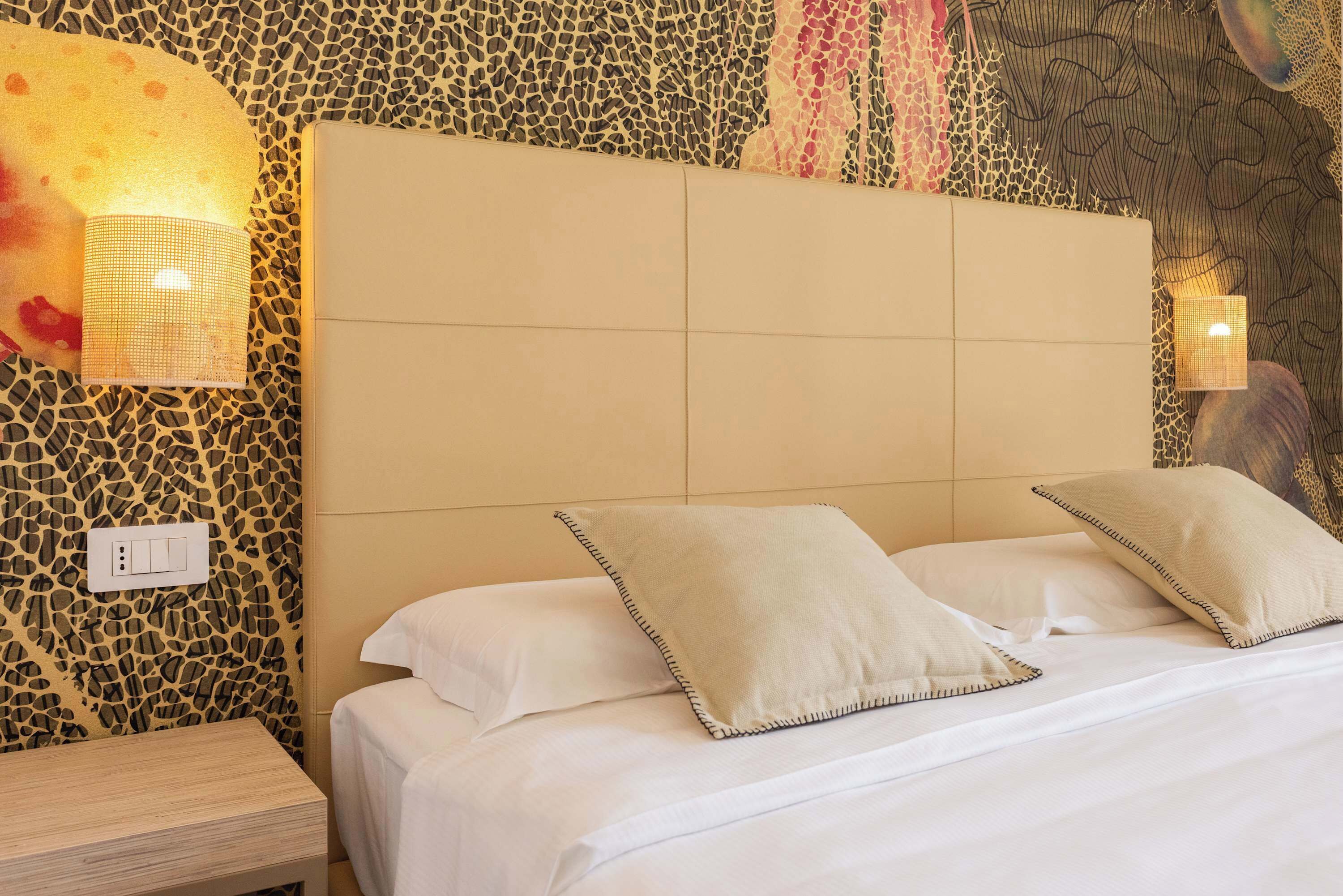 A bed with white linens and two pillows, a headboard with a textured pattern, and wall-mounted lamps.