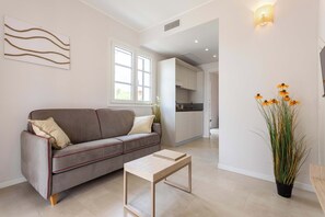 A modern living room with a sofa, a coffee table, a potted plant, and a kitchen in the background. - Appartamento "Isola di Marettimo 1" (Carini)