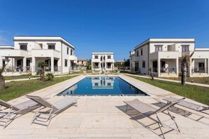 Ein Poolbereich mit Liegestühlen, einem klaren, blauen Pool und modernen Gebäuden mit Balkonen.