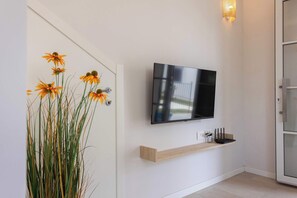 A modern interior with a mounted TV, a wooden shelf, and a door with a plant. - Appartamento "Isola di Marettimo 1" (Carini)