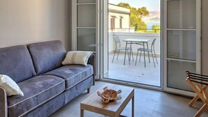 A modern living room with a grey sofa, a small wooden coffee table, and a sliding glass door leading to an outdoor seating area with a table and chairs. - Appartamento "Isola di Vulcano 2" (Carini)