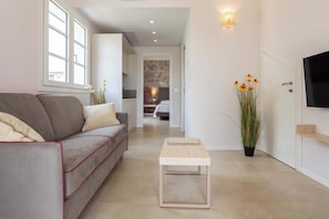 Una sala moderna con un sofá gris, una pequeña mesa de madera, un televisor montado en la pared y una planta en maceta.