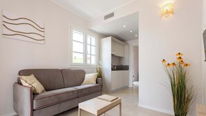 A modern living room with a sofa, a coffee table, a potted plant, and a kitchen in the background. - Appartamento "Isola di Alicudi 1" (Carini)