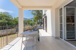 A balcony with a table and chairs, a glass door, and a view of trees and mountains. - Suite "Isola di Linosa 1B" (Carini)