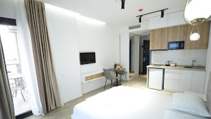 Una habitación de hotel con cama, escritorio con silla, kitchenette y televisión.