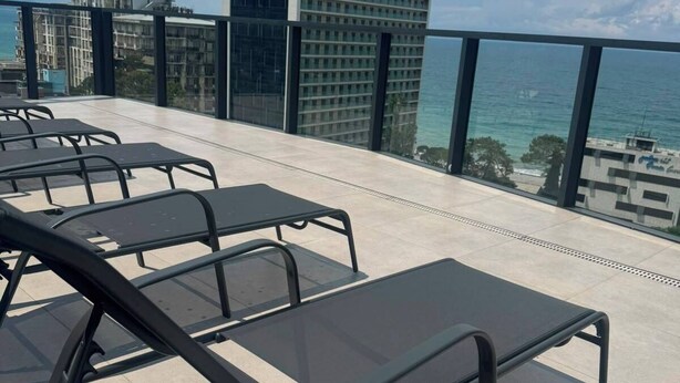 Terraza en la azotea con tumbonas y vista al océano y un rascacielos.