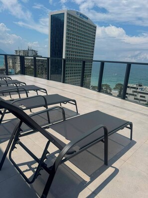 Une terrasse sur le toit, dotée de chaises longues et offrant une vue sur l’océan et un immeuble de grande hauteur.