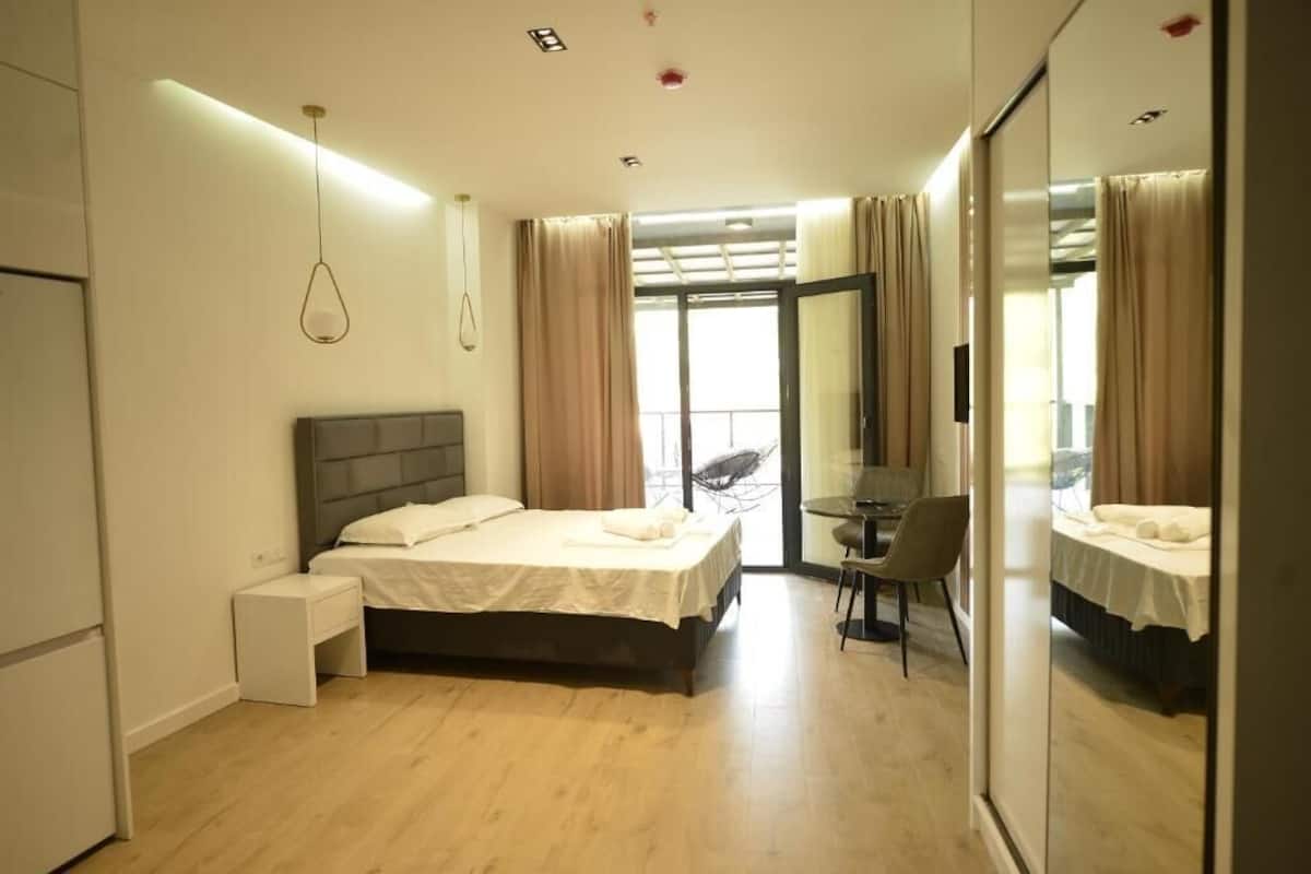 Una habitación de hotel moderna con cama, mesita de noche, silla y un espejo grande.