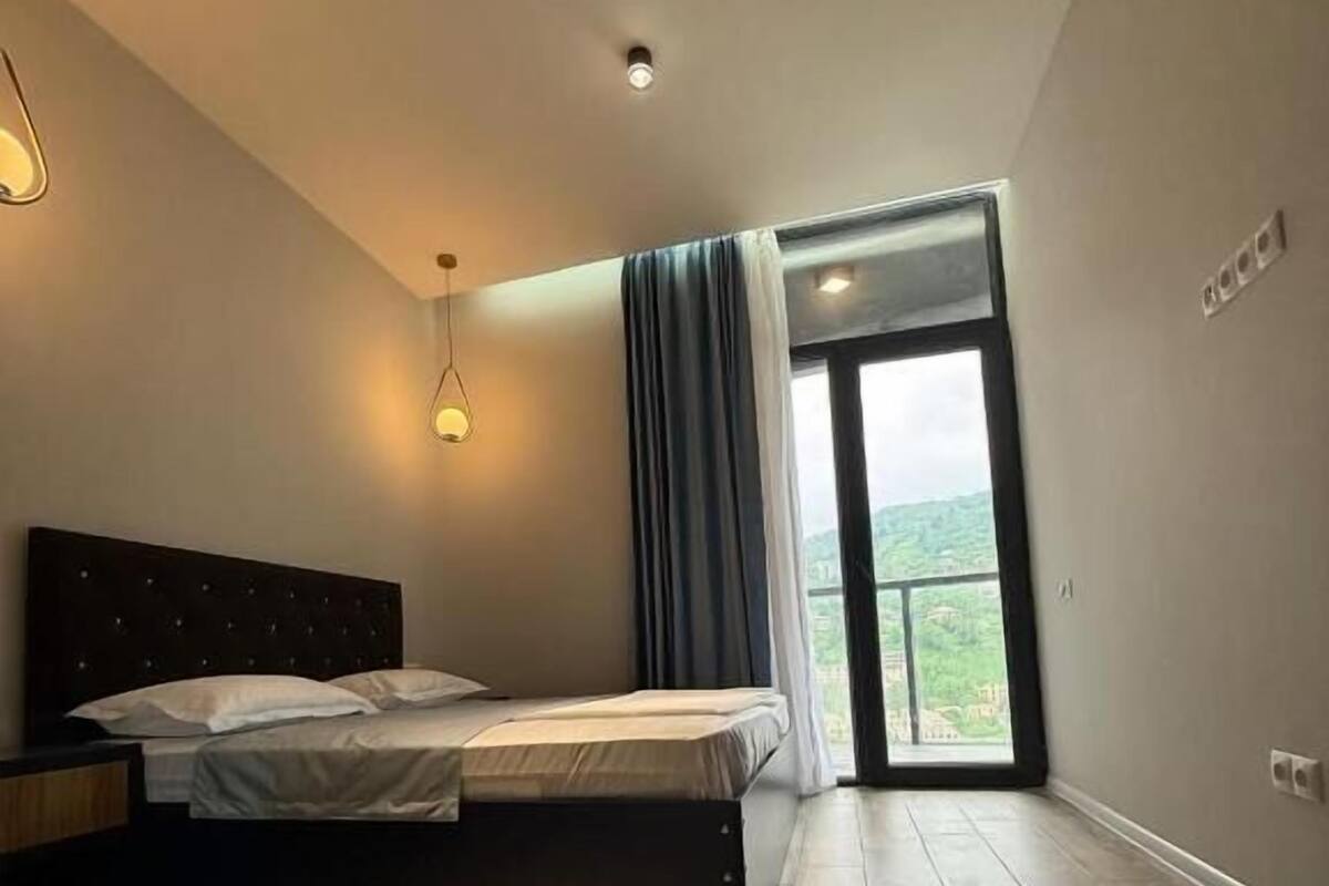 Un dormitorio con una cama, una mesita de noche, una lámpara de techo y vistas por una ventana.