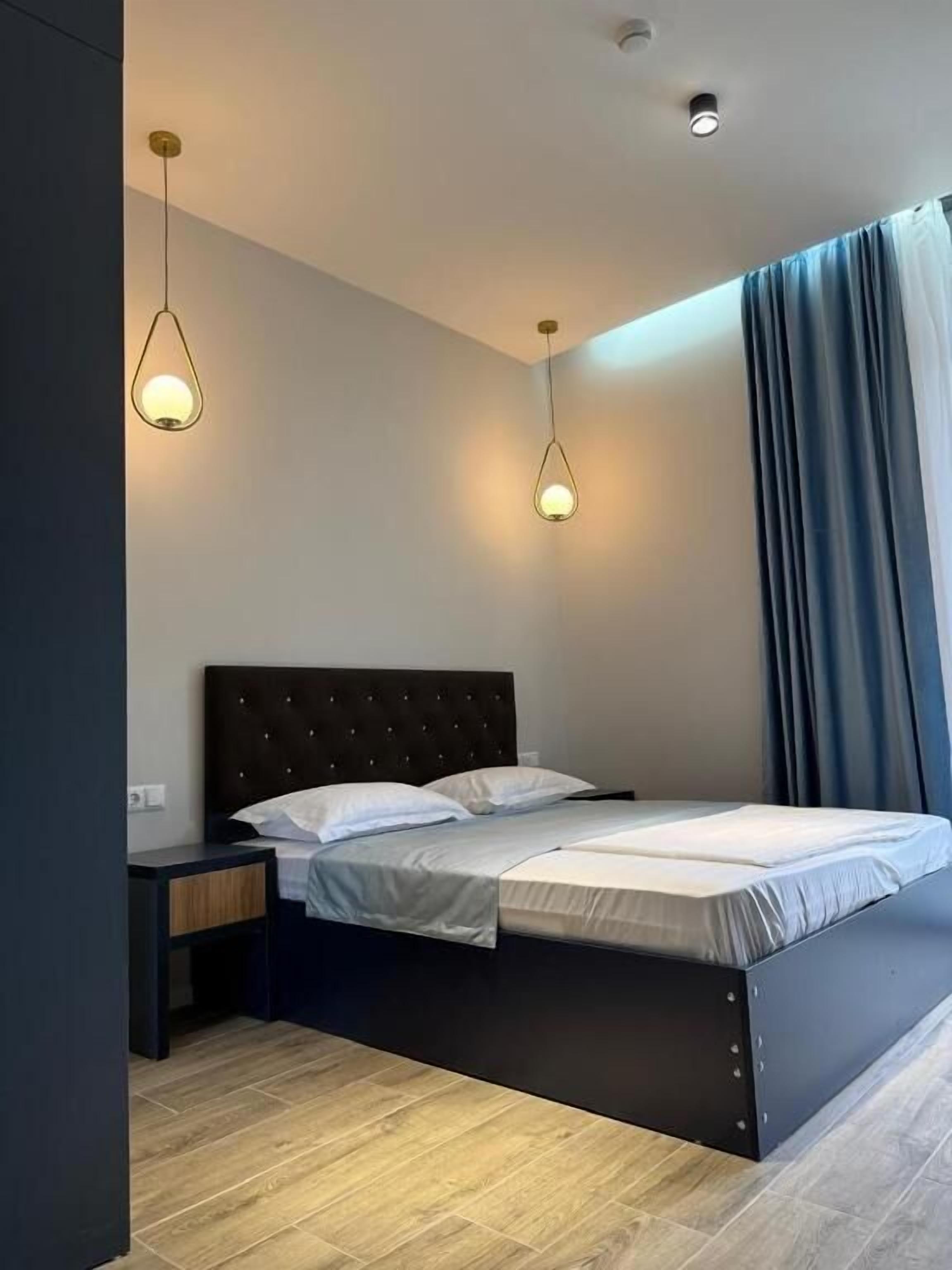 A modern bedroom with a bed, bedside tables, and pendant lights.