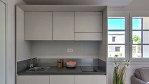 Eine moderne Küche mit einer zentralen Kochinsel, Deckenleuchten und Blick ins Freie durch große Fenster.