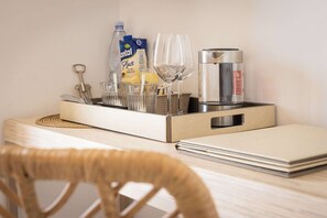 Une chambre d’hôtel avec une table en bois, un plateau avec des verres, des couverts, une bouteille, un verre à vin, un thermos et un carnet.