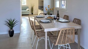 A dining area with a table set for four, surrounded by wicker chairs, with a view of the kitchen and a living area in the background. - Appartamento "Isola di Stromboli 2" (Carini)