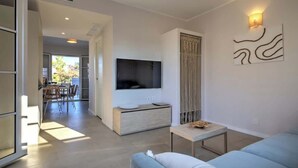 A modern living room with a sofa, a TV mounted on a wall, a small table, and a dining area in the background. - Appartamento "Isola di Stromboli 2" (Carini)