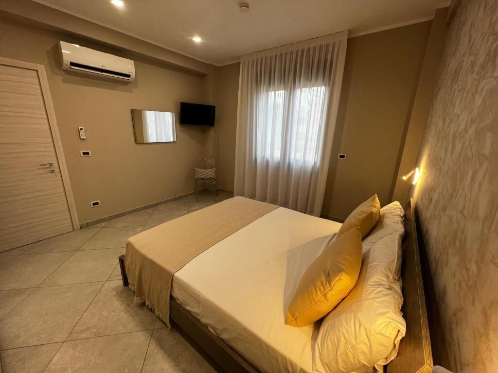 Un dormitorio con cama, cortinas, televisor montado y aire acondicionado.