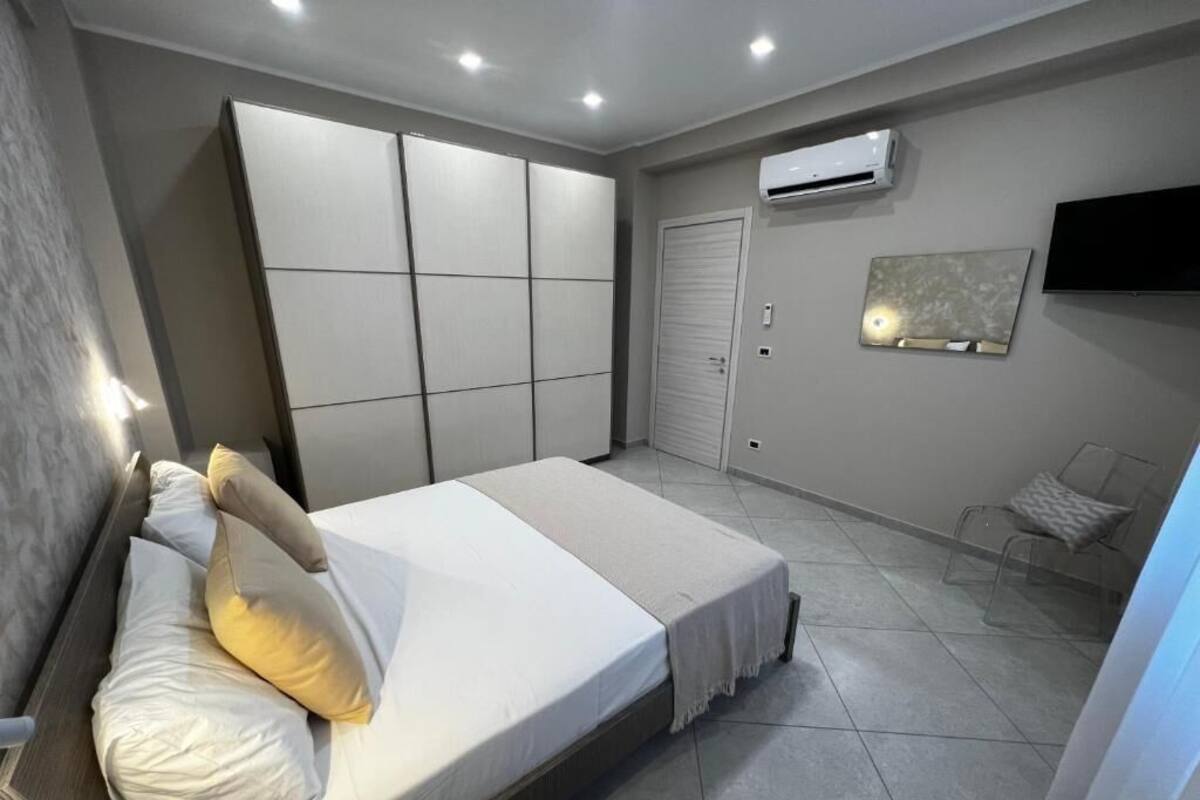 Ein Schlafzimmer mit Bett, Kleiderschrank, Klimaanlage, Fernseher und einem Sessel.