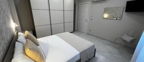 A bedroom with a bed, wardrobe, air conditioning unit, television, and a chair.