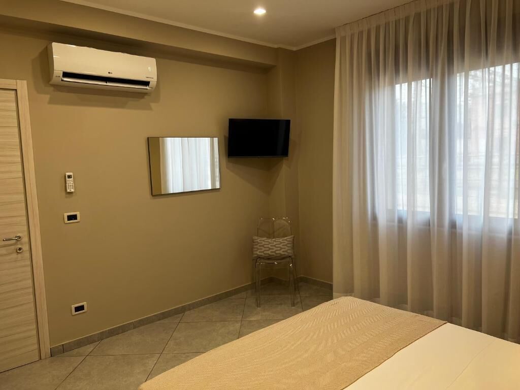 A hotel room with a bed, an air conditioning unit, a television, a chair, and a window with curtains.