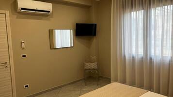 A hotel room with a bed, an air conditioning unit, a television, a chair, and a window with curtains.