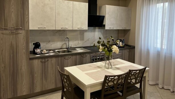 A modern kitchen with wooden cabinets, a built-in stove, and a dining area with a table and chairs. - B&B Lamezia Central Airport (Lamezia Terme)