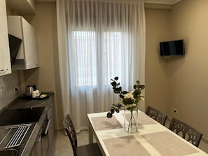 Un comedor con una mesa, sillas, un florero con flores, un televisor en la pared y una zona de cocina con armarios y un lavamanos.