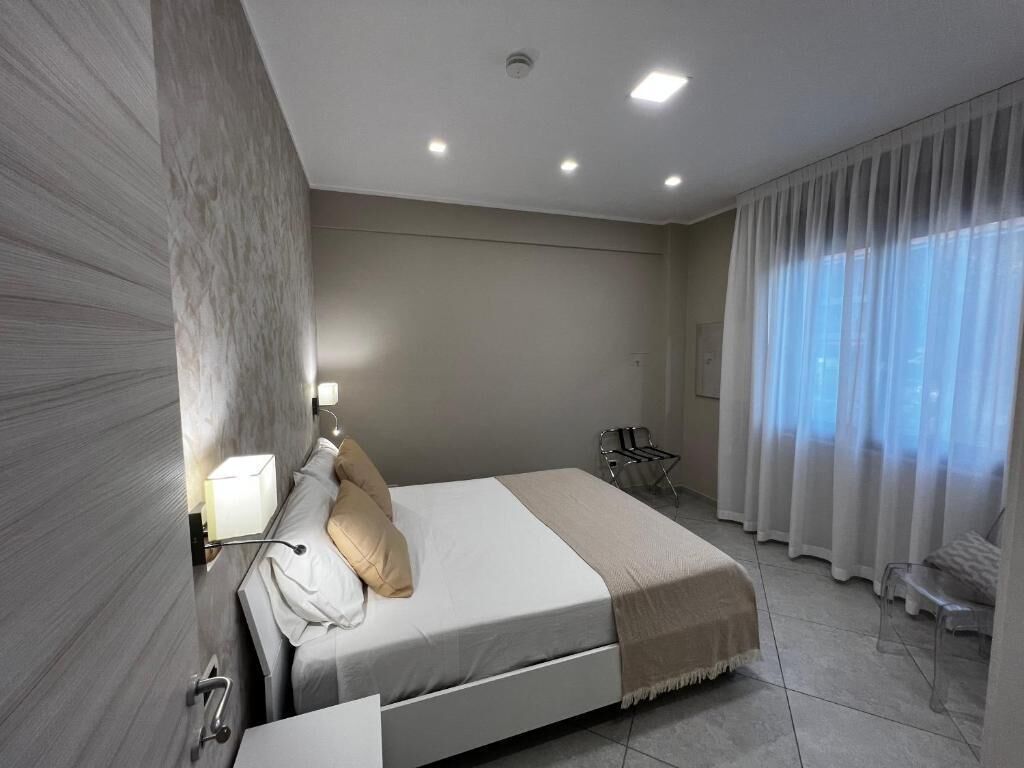 A modern bedroom with a bed, bedside table, lamp, and a view of the outdoors through sheer curtains.