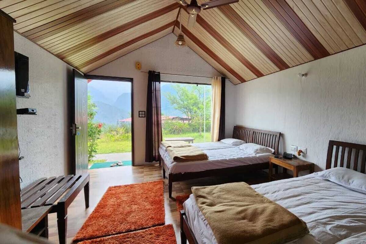 Quarto com duas camas, um banco, teto de madeira e vista para o exterior.