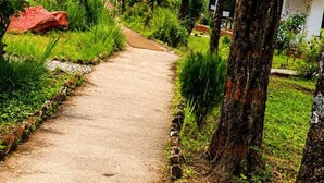 A pathway leading through a lush garden with trees and a building with red roofs in the background. - Chardham Resort Guptakashi (Ukhimath)