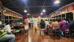 A restaurant with wooden floors, metal chairs, and tables. People are seated and standing, eating. - Chardham Resort Guptakashi (Ukhimath)