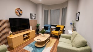 Una sala moderna con un televisor de pantalla plana, un mueble de madera para equipo multimedia, una mesa redonda de centro y dos sofás.