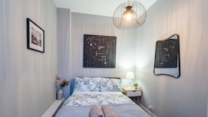 Una cama bien hecha con una colcha estampada, una mesita de noche con lámpara y dos obras de arte abstracto en la pared.