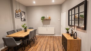 Un comedor con una mesa de madera, sillas grises, un radiador, un mueble de madera y estantes con plantas.