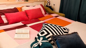 A neatly made bed with a variety of pillows and a rolled towel, a bedside table with a book and a bottle, a mirror, and a shelf with personal items. - Studio with double bed 5 minutes from Florence Campo di Marte station (Firenze)