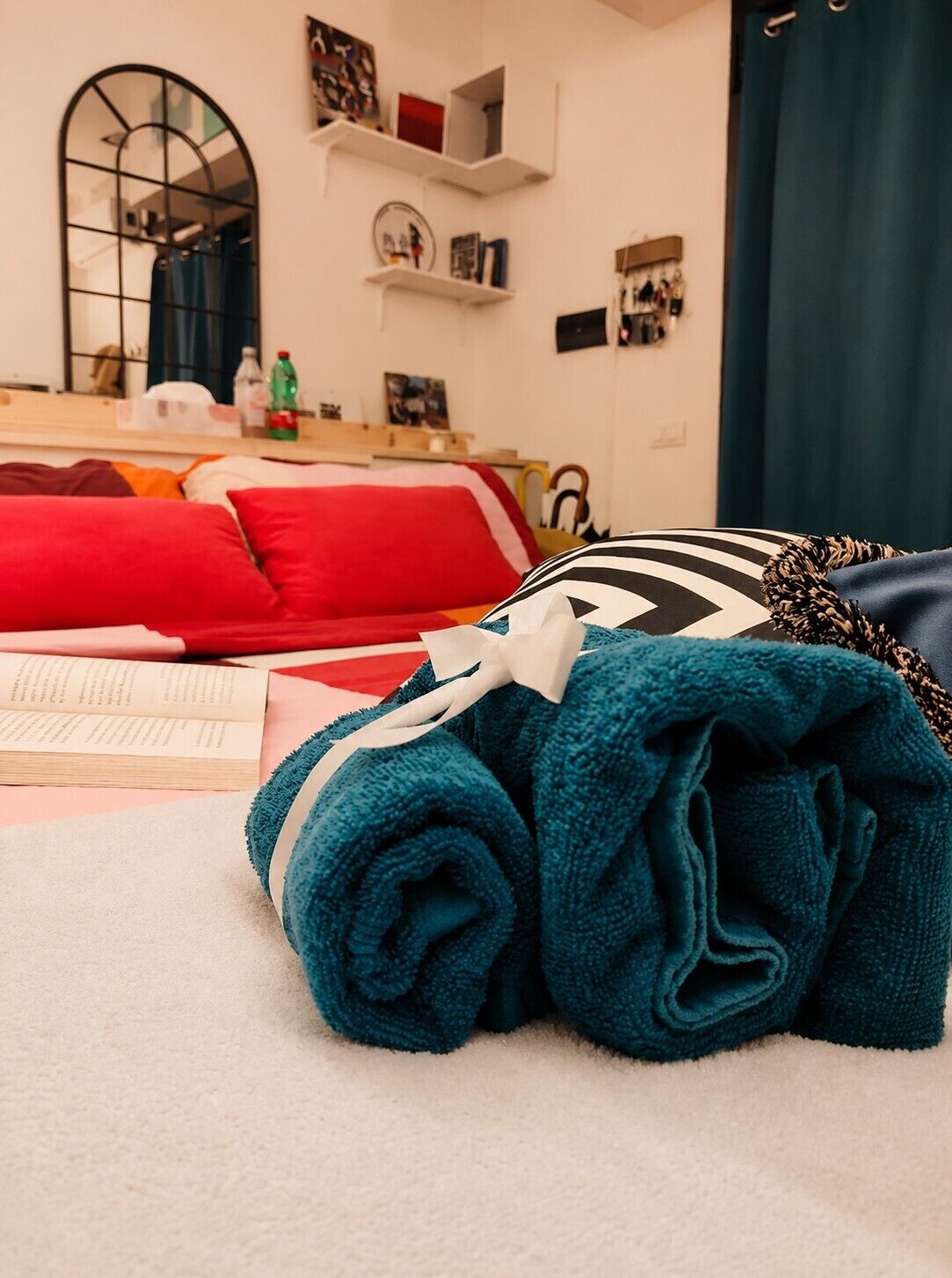 A neatly made bed with a red and white striped pillow, a rolled-up teal towel, and a striped pillow on a white bedspread.