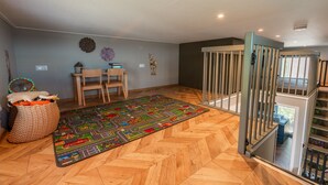 A room with a herringbone wooden floor, a colorful play mat, a desk with chairs, a basket with toys, and a wall-mounted decoration. - De Wiedense Meren - Villa Waterrijk MIVA | 3p (Wanneperveen)