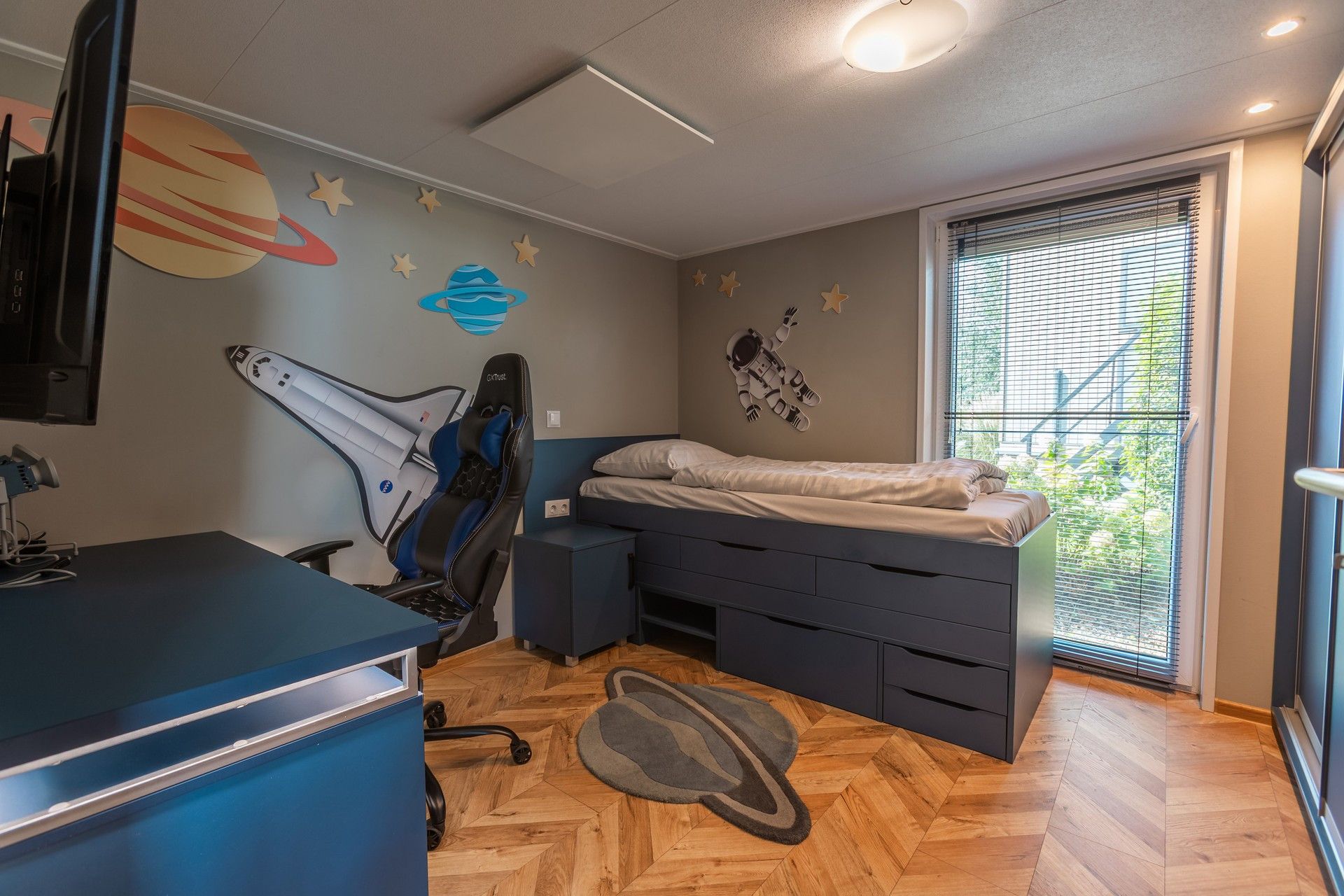 A bedroom with a bed, desk, chair, and a window with blinds.