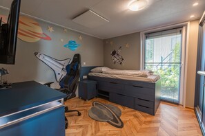 Ett sovrum med en säng, ett skrivbord, en stol och ett fönster med persienner.