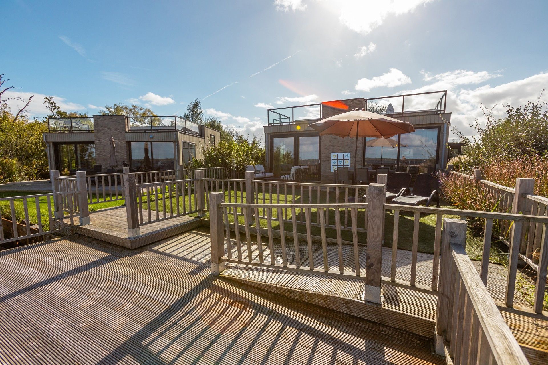 Eine moderne Terrassengestaltung im Freien mit Holzgeländern und einer Glasverkleidung, ausgestattet mit Sitzgelegenheiten und Blick auf die umliegende Landschaft.
