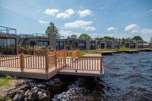 A modern waterfront property with a wooden deck, glass windows, and a stone facade.